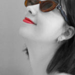 Black and white profile of a person looking up with a color pop on the brown cat eye sunglasses by Laurie Olefson as well as the bright red lipstick