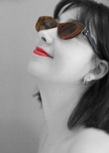 Black and white profile of a person looking up with a color pop on the brown cat eye sunglasses by Laurie Olefson as well as the bright red lipstick