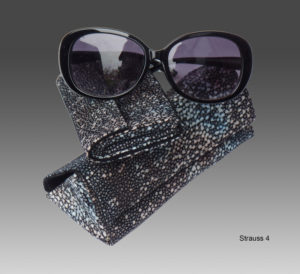 Black sunglasses laid on two matching fish leather eyeglass cases in grey