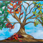 Stained glass panel by Jill Tarabar of a tree with long branches of green and red leaves