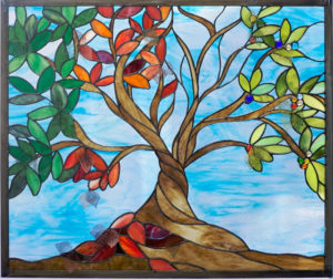 Stained glass panel by Jill Tarabar of a tree with long branches of green and red leaves