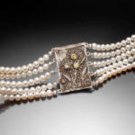 Bracelet by Judith Hearney with four rows of pearls to wrap around the wrist and in the center, a metal plate with sunflowers holding semiprecious stones.