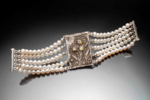 Bracelet by Judith Hearney with four rows of pearls to wrap around the wrist and in the center, a metal plate with sunflowers holding semiprecious stones.