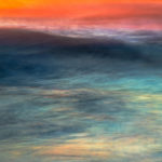 Photograph taken by Frederick Ballet of a rich seascape with both light and deep blues with a orange and pink sunset reflecting on the water.