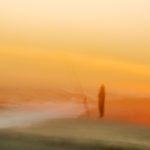 Photograph by Frederick Ballet of a shifting silhouette of a person and fishing rod right on the edge of the ocean's tide in an orange sunset.