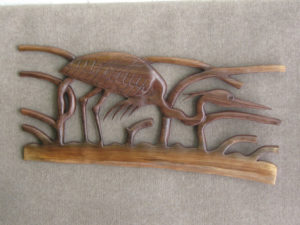 A carved wooden piece by Gilbert Carey depicting a crane crouching behind reeds.