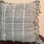 A grey pillow with fringe by Belinda DeCicco.