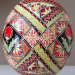 A large pysanky by Marino Diaz. The egg is full of flower, poppy, and triangle motifs in green, red, yellow, and black,