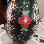 A pysanky by Marino Diaz. The egg is black with green vines and a red flower in the center and diamond patterns surrounding.