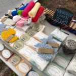 A sign that says "Handmade Vegan Soaps" on a table with a collection of different scented soaps and loofahs from the LEH Soap Company.