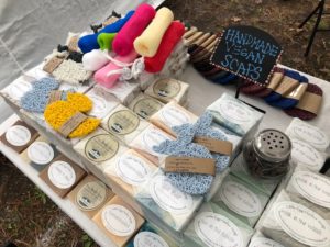 A sign that says "Handmade Vegan Soaps" on a table with a collection of different scented soaps and loofahs from the LEH Soap Company.