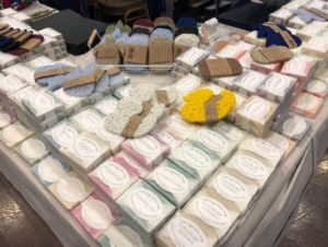 A table with a collection of different scented soaps and soap holders from the LEH Soap Company.