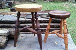 Two wooden benches, one dark brown with a light tan seat and the other a medium tan with a dark brown seat. Created by Thomas Ferrie.