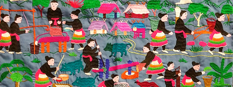 An embroidered story cloth by Pang Xiong Sirirathasuk Sikoun. The cloth depicts scenes of life, such as cleaning and cooking, throughout the cloth.