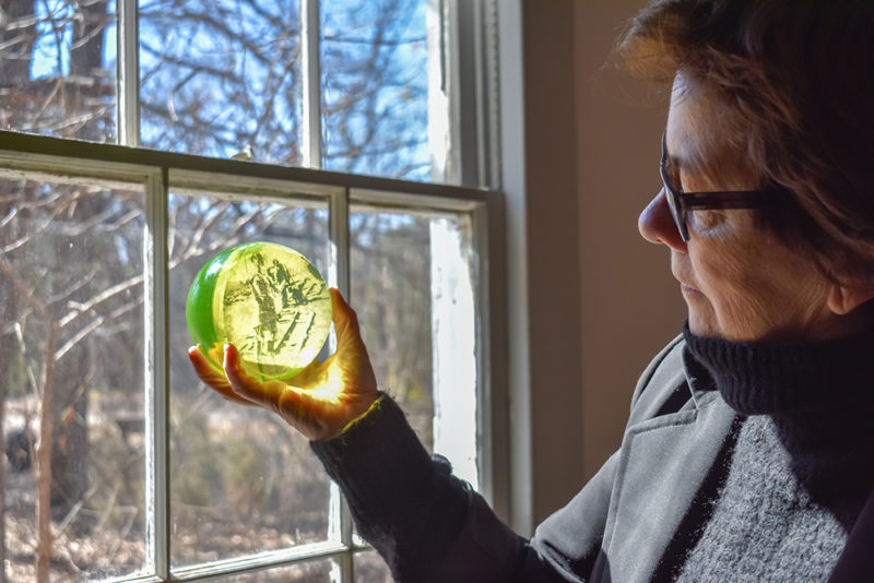 Emanation 2019 artist Jo Yarrington looks pensively at a uranium glass sphere as it catches the light from a nearby window