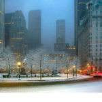 Photograph by Michael Leu of a city scene dusted in white snow, highlighted by the yellow lights from the lampposts and the bright red tail lights of passing cars.