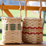 Two woven baskets by Mary May on a bench, one with green accents woven through and one with two red stripes woven through.