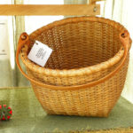 A large woven basket by Mary May with a large wooden handle.