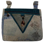 A grey and blue patterned purse with a prussian blue trim and a deep v on the front. Created by Agustin Ruiz.