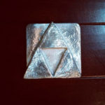 A triforce or Mitsuuroko symbol formed within a metal square. Created by Rachel Marie Wenner.