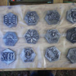 12 metal hexagons with various designs laid onto a wooden table. Created by Rachel Marie Wenner.