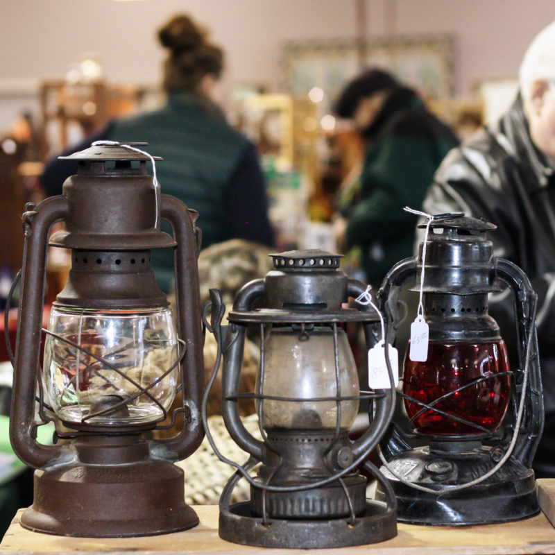 A collection of 3 old lanterns with customers in the blurred background.
