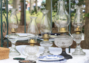 A collection of 5 glass oil lamps surrounded by china plates.