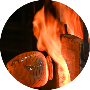 Glass vase going into a flaming glory hole.