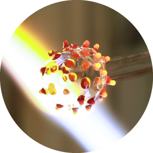 Circle cutout of flameworked glass in front of a torch flame.