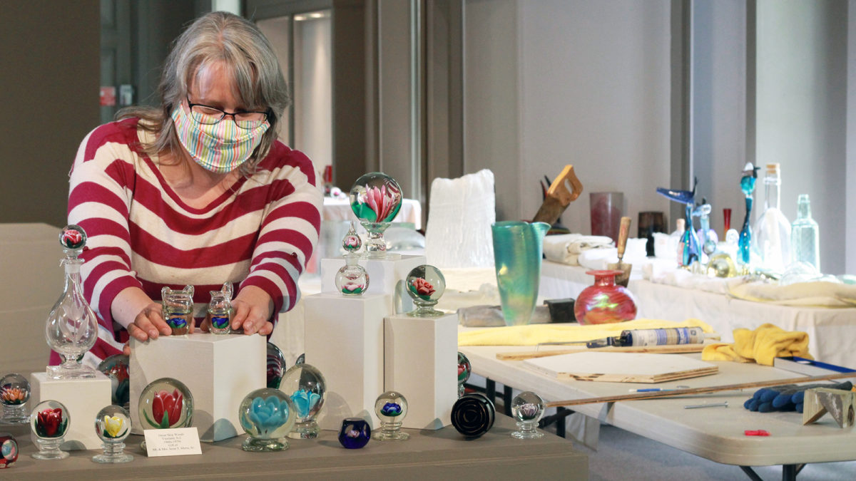 Kristin Qualls, Director of Exhibitions and Collections, sets up a display of various glass paperweights.