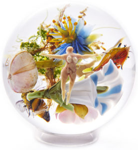 A paperweight by Paul Stankard with a floating figure in front of a bundle of flowers in white, blue, pink, and orange.