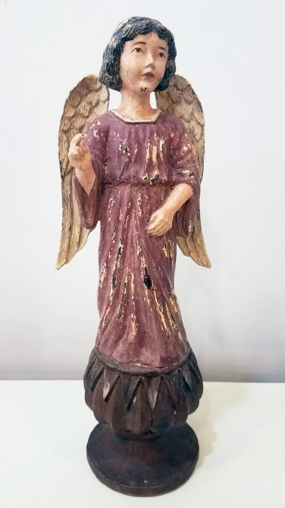 A carved and painted depiction of an angel with black hair and a red dress. She looks up to the sky.