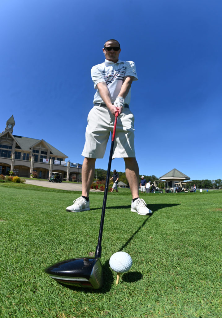 Man on golf grounds, ready to swing at golf ball.