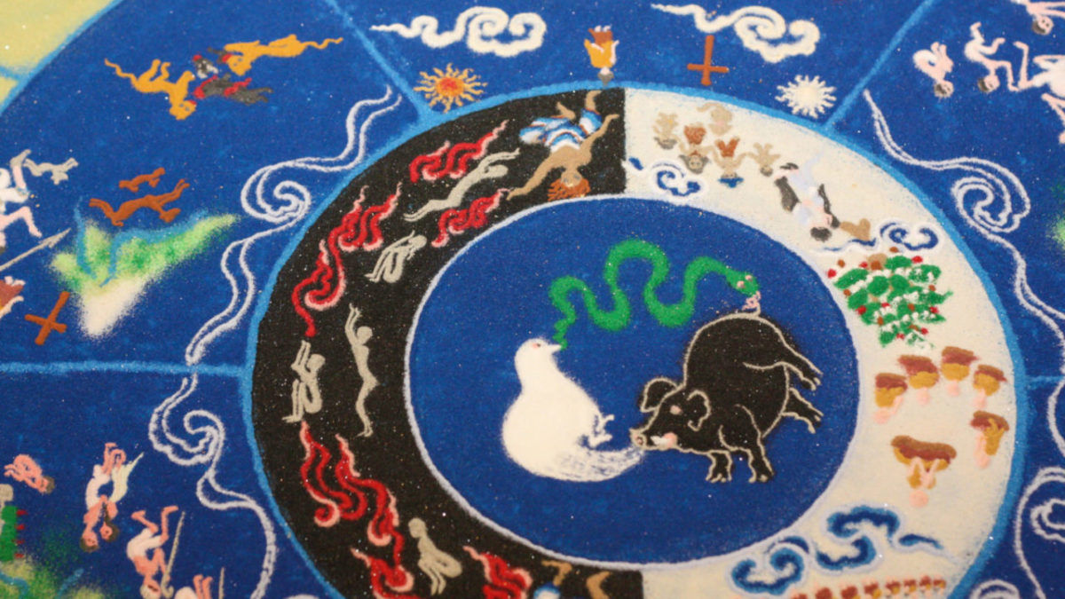 Sand mandala of the wheel of life with a pig, dove, and snake at its center.