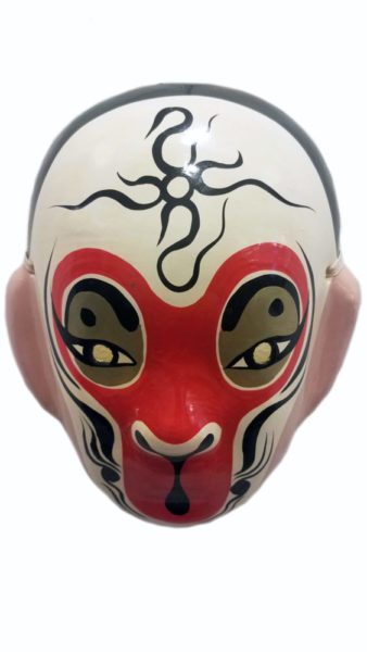 “Monkey King” Peking Opera Mask, artist unknown. Papier-mâché, acrylic paint. Collection of Peter Liu. The mask is white with a central red design surrounding the eyes, nose, and mouth. There are black line designs around the contours of the face and in the center of the forehead.