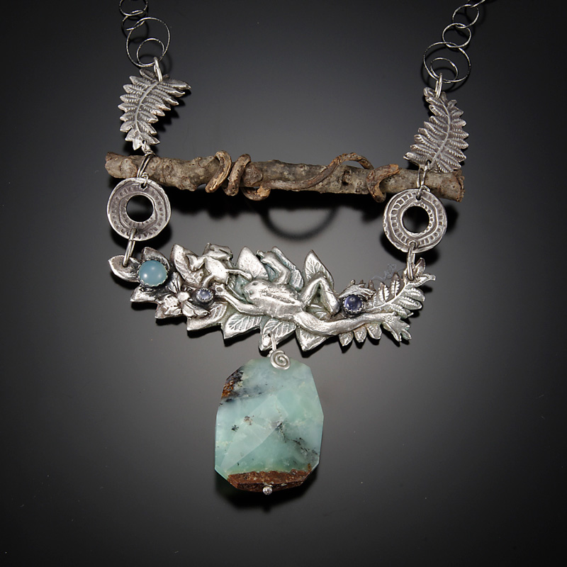 A necklace by artist Diana Contine. The necklace has silver leaves, a small brown branch, and a teal stone pendant in the center.