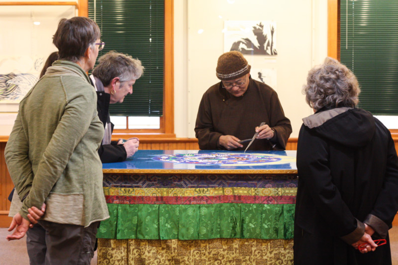 Artist Losang Samten creates a sand mandala as four visitors observe.