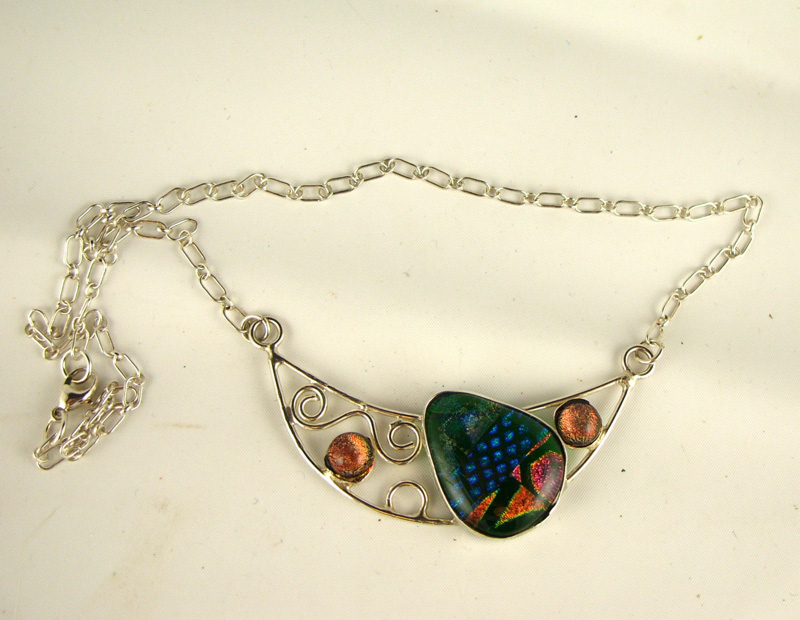 A necklace by artist Pamela Iobst. A long chain connects to a large multicolored stone, sitting within a wire semicircle.