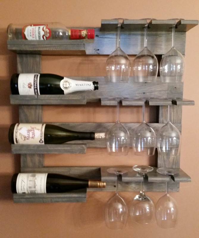 A light gray wine rack by Sharon Knapp holds four wine bottles on their sides to the left. To the right, three rows of wine glasses hang upside-down in their slots.