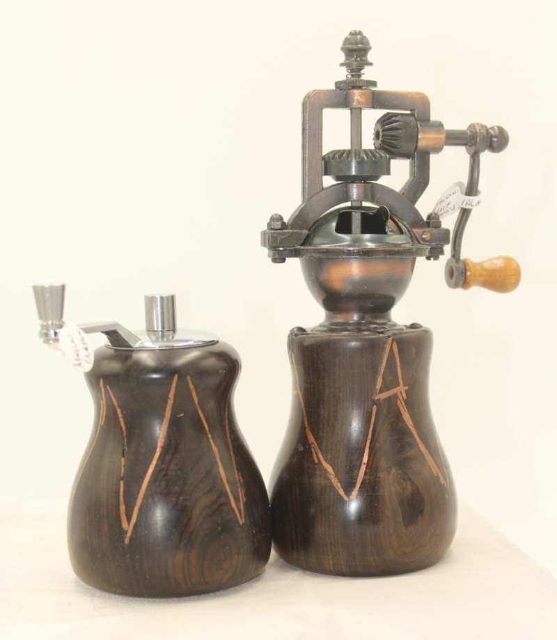 A pair of salt and pepper mills. The mills have similar designs, both a deep brown with an orange, carved out zigzag design. The mill on the left has a short silver grinder on top. The mill on the right is much taller with a vertical crank.