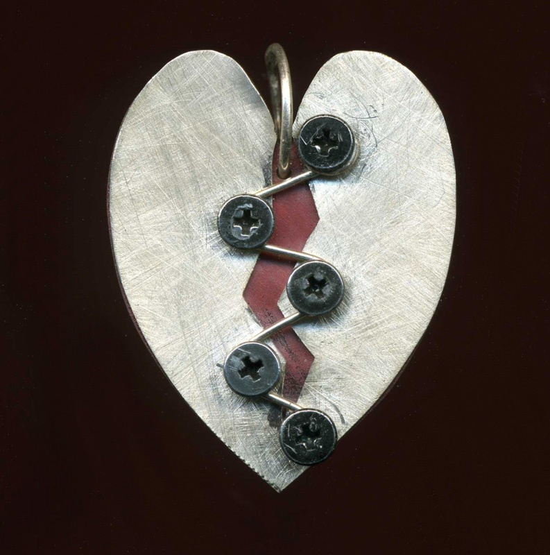 A pendant by jewelry artist Anthony Niglio. The silver pendant is shaped like to halves of a silver heart, stitched together with screws and wire. Behind the silver halves, a deep red color pokes through.