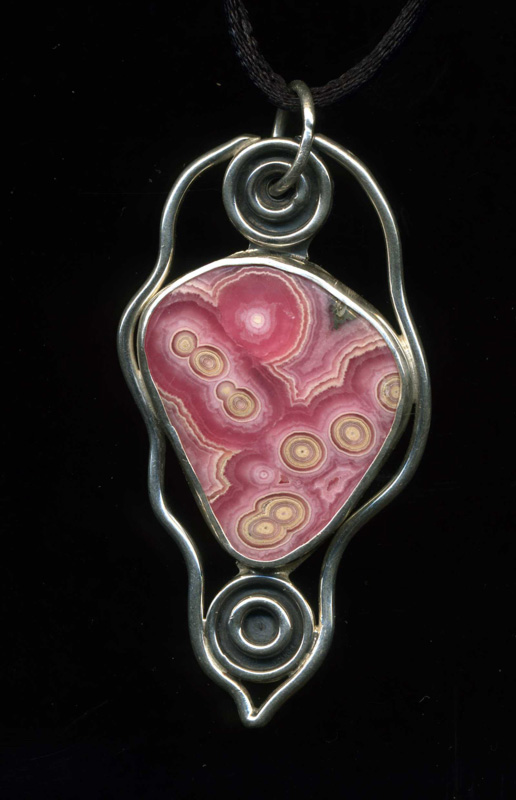 A pendant by jewelry artist Anthony Niglio. The pastel pink stone pendant is framed by a silver wire.