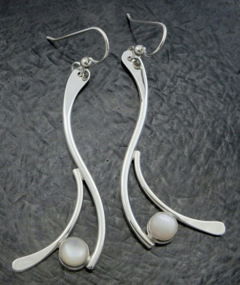 A pair of earrings by artist Ted Walker. Each silver earring has two long curved lines with two branched off ends. Each end holds a small pearlescent bead.