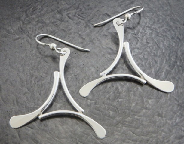 A pair of earrings by artist Ted Walker. Each earring has three curved silver lines connecting to create a concaved triangle shape.