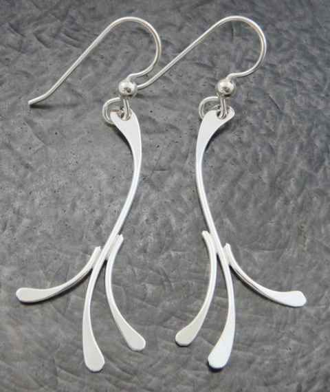 A pair of earrings by artist Ted Walker. Each earring is a long and curved silver shape, branching off into three separate ends.