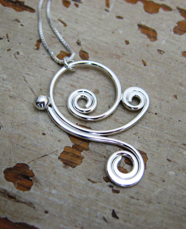 A pendant by artist Ted Walker. The long silver pendant spirals several times to create a charming design.