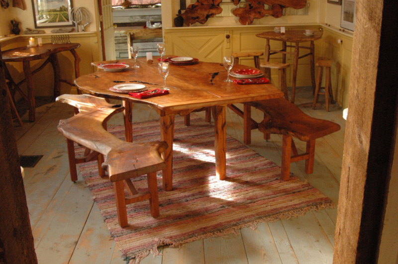 Two naturally shaped, long wooden benches sit on either side of a similarly natural, long wooden table, made by artist Abe Warren.