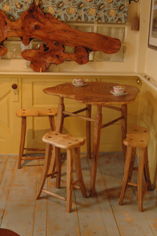 Three wooden stools surround a small wooden table with a natural tabletop, made by artist Abe Warren.