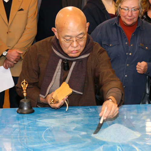 Artist Losang Samten begins a sand mandala as a group of visitors oberves.