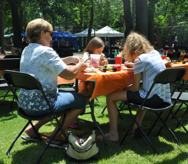 Three people enjoy the craft station on a sunny day at the Fantasy Faire